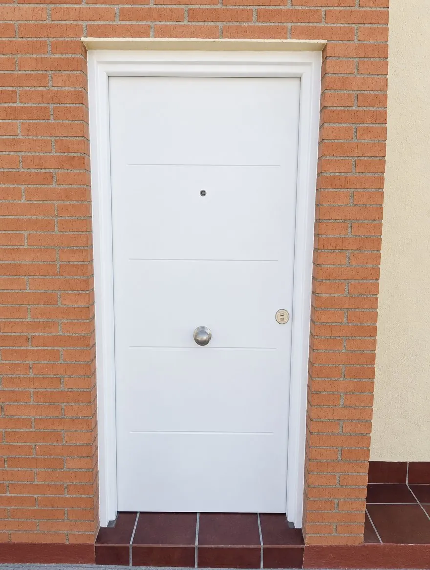 THT Saga 100 blanca con cuatro líneas horizontales y pomo central, en la entrada de ladrillo de una casa